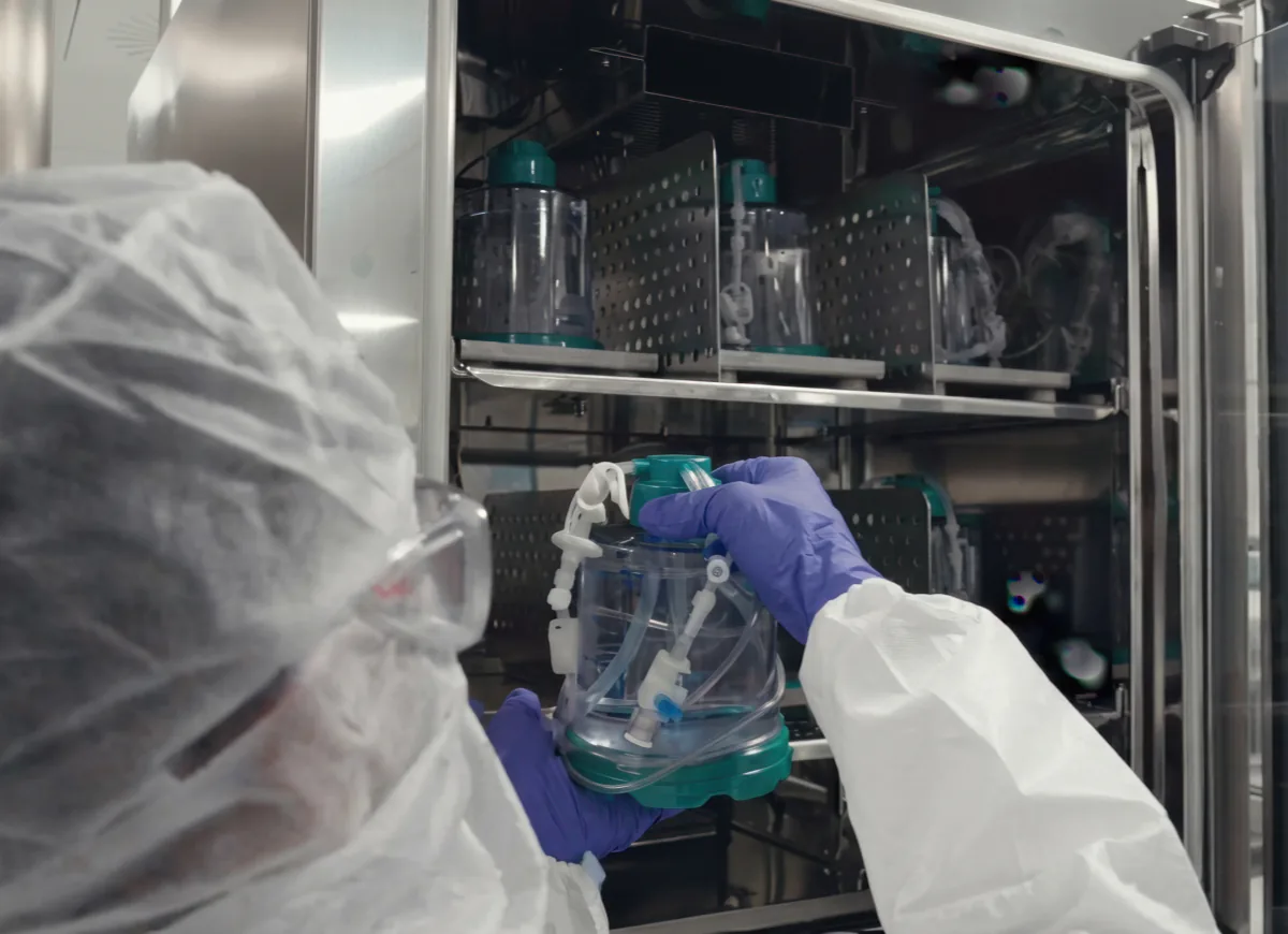 An operator in a cleanroom holding a G-Rex bioreactor in front of an incubator loaded with G-Rex units